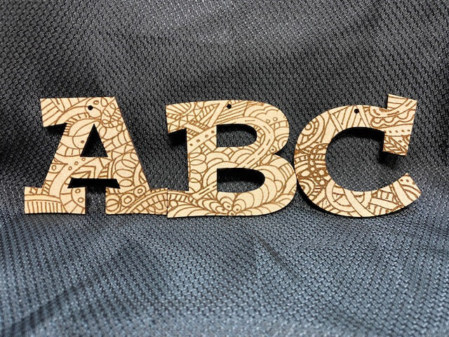 Wooden letters 'A', 'B', and 'C' with intricate patterns on a textured gray background