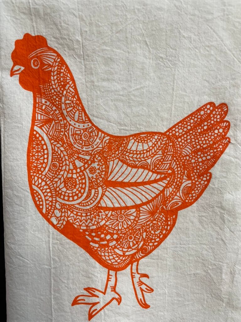 A tea towel with an orange and white design featuring a hen.