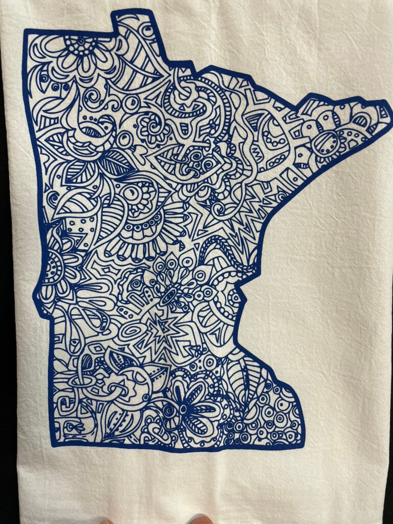 A tea towel with a state shape of Minnesota in blue color, decorated with a floral and geometric pattern.