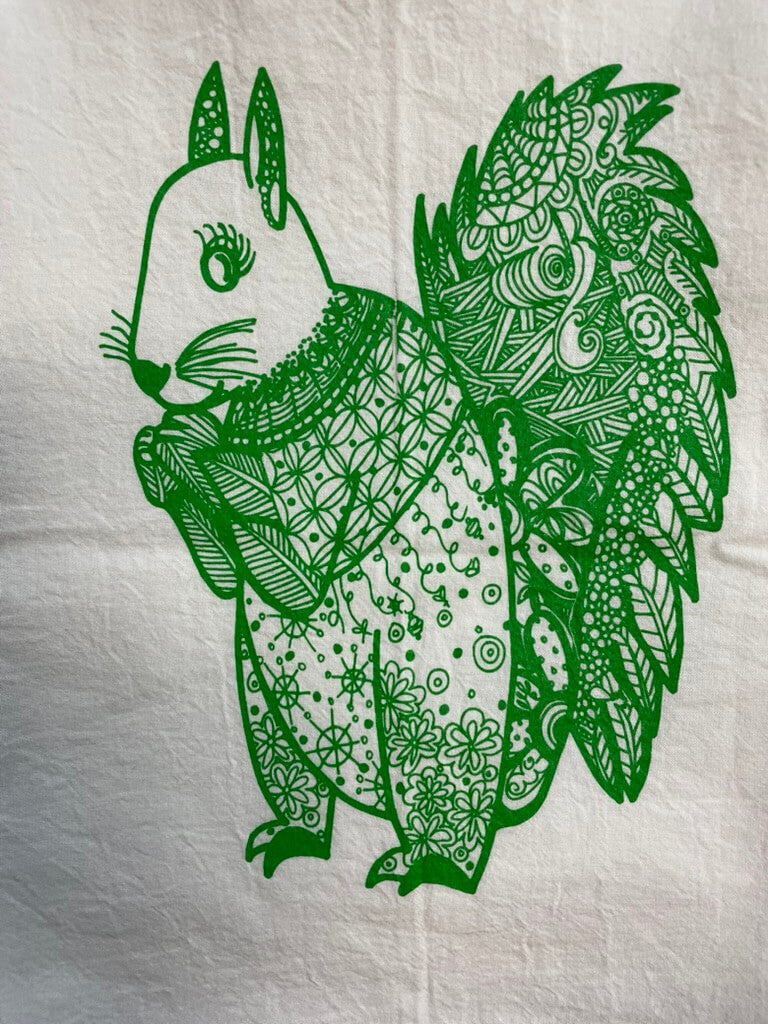 A tea towel with an green and white design featuring a squirrel.
