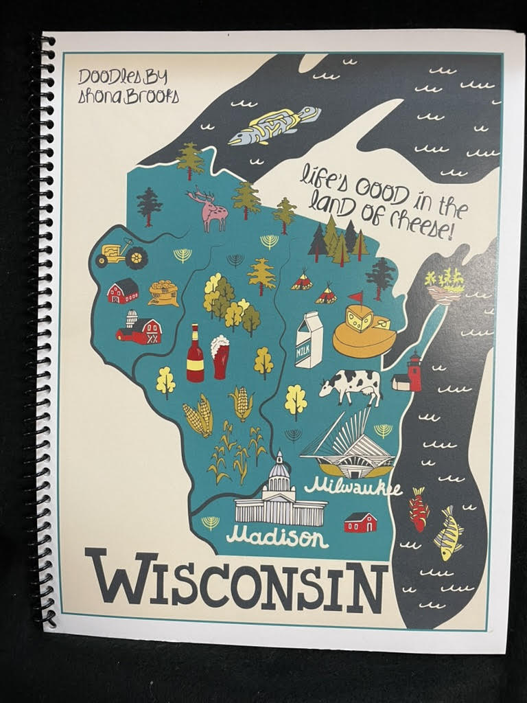 Illustrated map of Wisconsin on a notebook cover with text 'Life's good in the land of cheese!'.