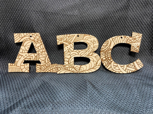 Wooden letters 'A', 'B', and 'C' with intricate patterns on a textured gray background
