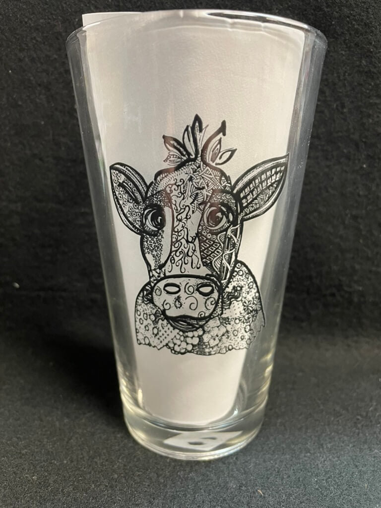 A clear glass pint with a cow design on the side.