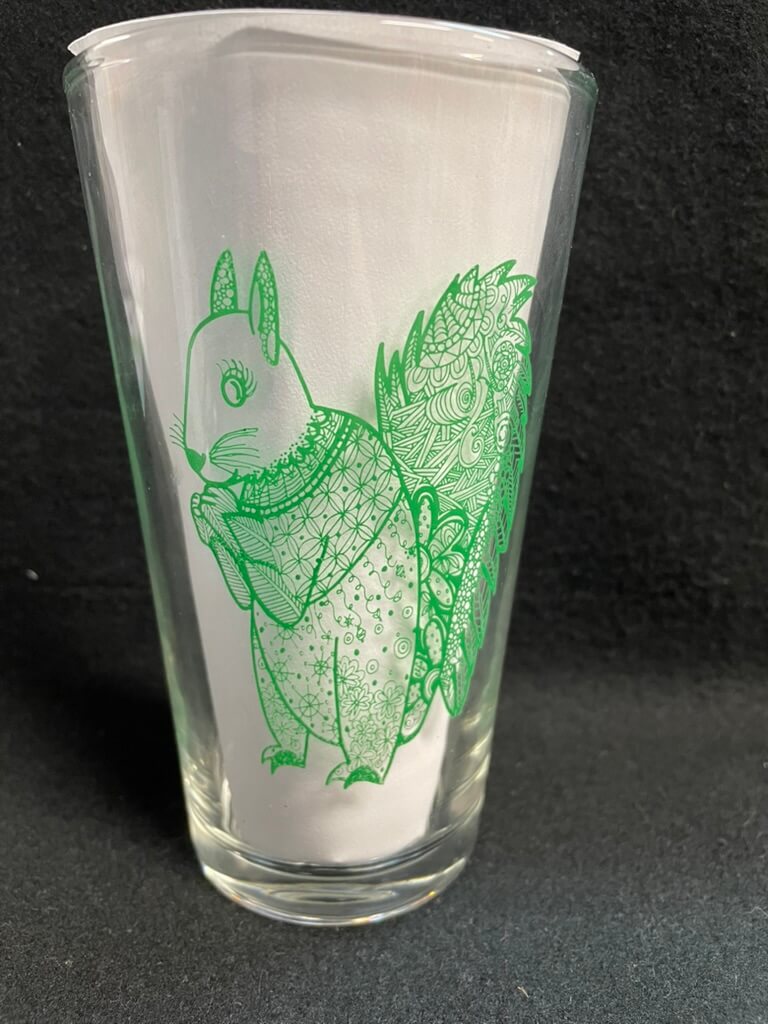 A clear pint glass with a green squirrel design.